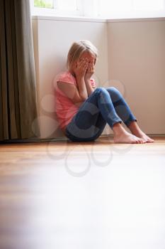 Unhappy Child Sitting On Floor In Corner At Home