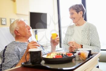 Senior Couple In Hospital Room As Male Patient Has Lunch