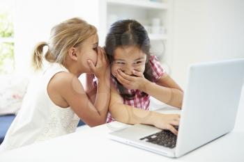 Two Young Girls Using Laptop At Home And Whispering