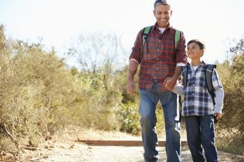 Father And Son Hiking In Countryside Wearing Backpacks