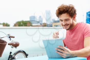 Young Man Sitting On Roof Terrace Using Digital Tablet
