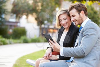 Business Couple Using Digital Tablet On Park Bench