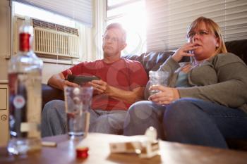 Couple Sitting On Sofa With Bottle Of Vodka And Cigarettes