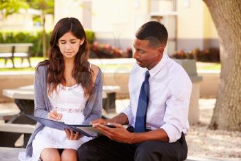 Teacher Sitting Outdoors Helping Female Student With Work