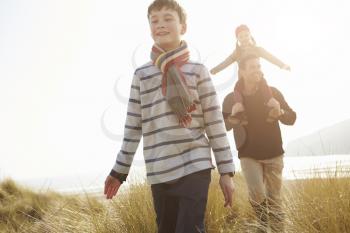 Father And Children Walking Through Dunes On Winter Beach