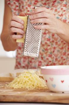 Close Up Of Woman Grating Cheese In Kitchen
