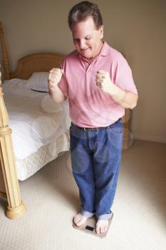 Happy Overweight Man Standing On Scales In Bedroom