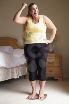 Overweight Woman Weighing Herself On Scales In Bedroom