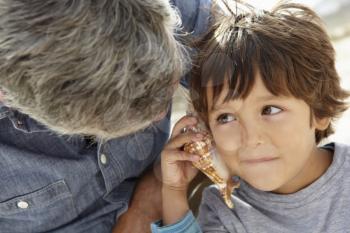 Young boy listening to seashell with grandfather