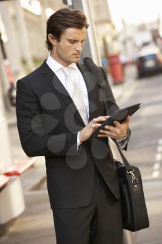 Businessman standing at bus stop using tablet