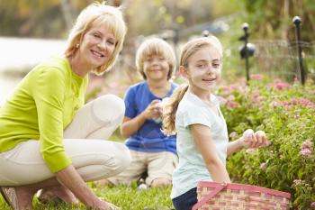 Grandmother With Grandchildren On Easter Egg Hunt In Garden