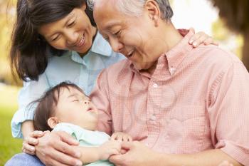 Grandparents Holding Sleeping Grandson In Park