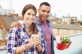Couple Relaxing Outdoors On Rooftop Garden Drinking Coffee