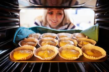 Woman Putting Cupcakes Into Oven To Bake