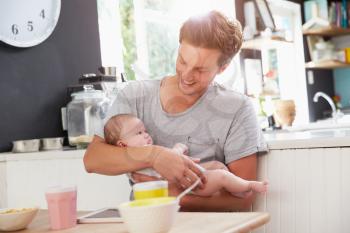 Father Holding Newborn Baby Daughter At Kitchen Table