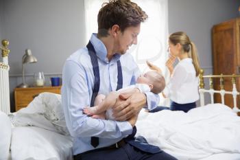 Parents With Young Baby Dressing For Work In Bedroom