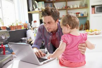 Father With Young Daughter Using Laptop In Kitchen