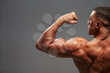 Male bodybuilder flexing bicep, back view with copy space