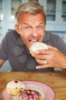 Mature Man Sitting At Table Eating Sugary Donut