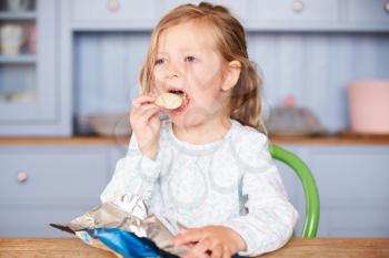 Young Girl Sitting At Table Eating Potato Chips