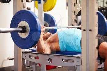 Young man bench pressing weights at a gym, side view