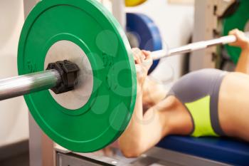 Young woman bench pressing weights at gym, focus on barbells