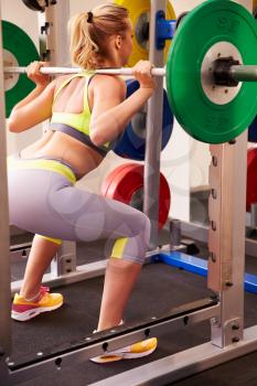 Woman weightlifting barbells at a squat rack in a gym