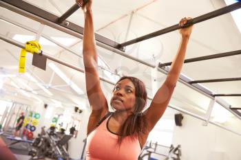 Young woman hanging from monkey bars at a gym