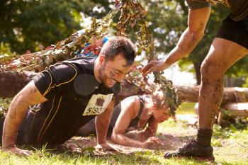 Assault course competitor helping others crawl under nets