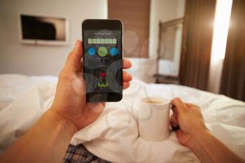 Man In Bed Looking At Health Monitoring App On Mobile Phone