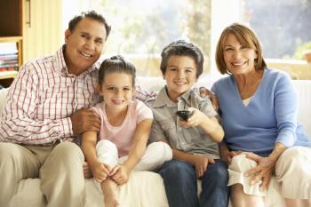 Hispanic Grandparents With Grandchildren Watching TV On Sofa At Home
