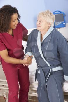 Nurse helping senior woman out of bed in hospital