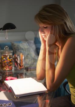 Unhappy Teenage Girl Looking At Diary In Bedroom At Night