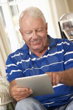 Retired Senior Man Sitting On Sofa At Home Using Tablet Computer