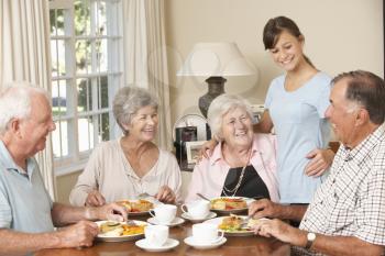 Group Of Senior Couples Enjoying Meal Together In Care Home With Teenage Helper