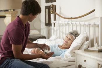 Teenage Grandson Giving Grandmother Medication In Bed At Home