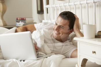 Man Using Laptop In Bed At Home