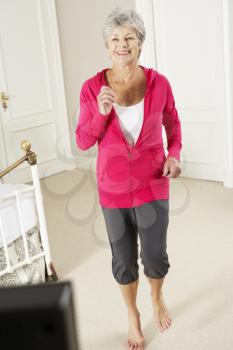 Senior Woman Exercising Whilst Watching Fitness DVD On Television