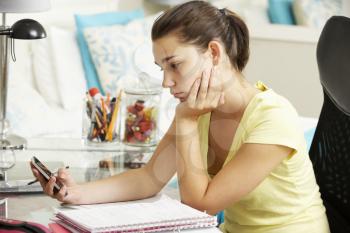 Unhappy Teenage Girl Studying At Desk In Bedroom Looking At Mobile Phone