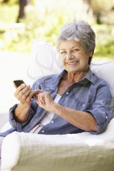 Senior Woman Sending Text Message Sitting On Sofa