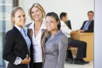Portrait Of Three Female Executives With Office Meeting In Background