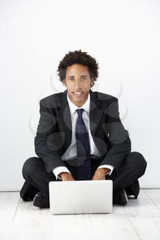 Studio Portrait Of Businessman Sitting On Floor Using Laptop