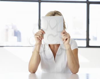Businesswoman Sitting At Desk In Office With Face Hidden Behind Digital Tablet