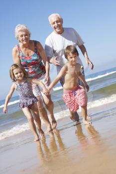 Grandparents And Grandchildren Running Along Beach