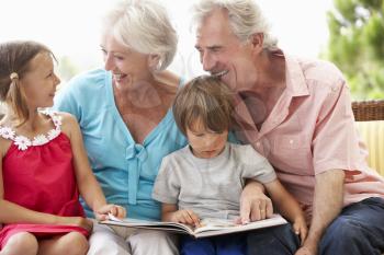 Grandparents And Grandchildren Reading Book On Garden Seat