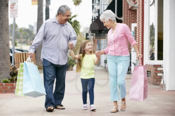 Senior Couple With Granddaughter Carrying Shopping Bags