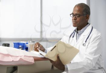 Male Doctor In Surgery Reading Patient Notes