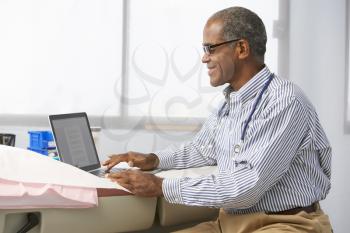 Male Doctor In Surgery Using Laptop