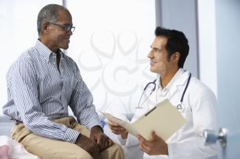 Doctor In Surgery With Male Patient Reading Notes