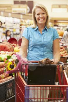 Woman Pushing Trolley By Fruit Counter In Supermarket